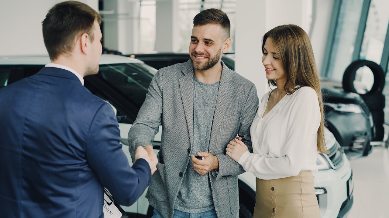 Home Happy couple finalizing car purchase with salesman in dealership showroom. Bright and welcoming environment.